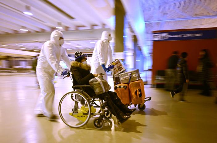 Workers wearing protective masks and suits help a Chinese traveler