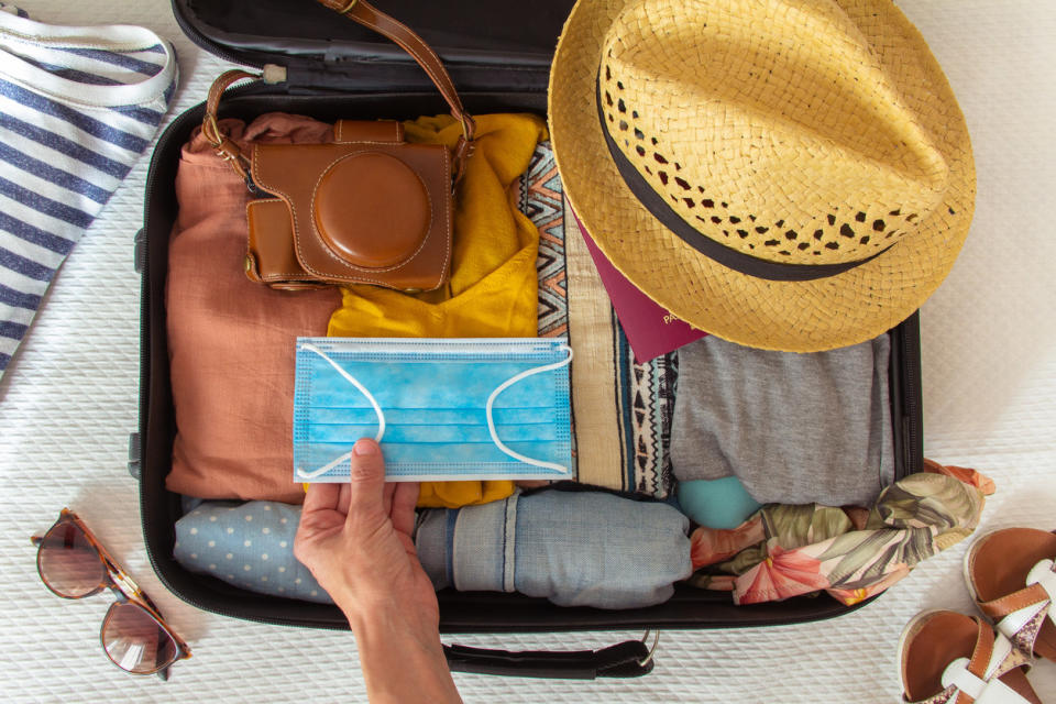 A small suitcase with packed clothes, a hat, sunglasses, and a mask