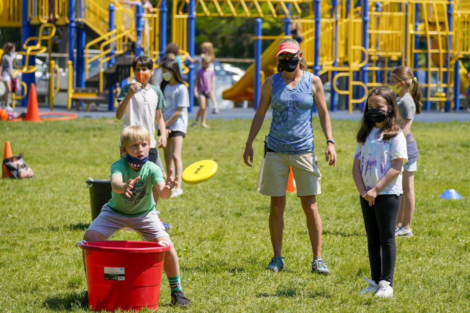 FILE - Gym teacher Becky Ward, center, watches as fifth graders throw frisbees at the Milton Elementary School, Tuesday, May 18, 2021, in Rye, N.Y. Gov. Andrew Cuomo said Monday that students no longer have to wear masks while outdoors on school grounds. But students and staff will still have to wear masks for the rest of the school year. (AP Photo/Mary Altaffer, File)