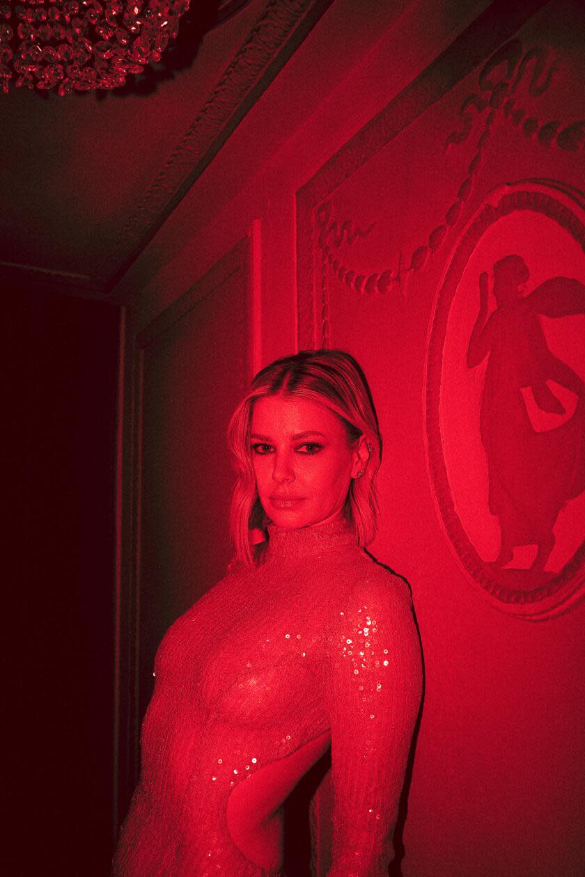 Ariana Madix leans against a wall at the Ambassador Theater in a red-lit portrait.