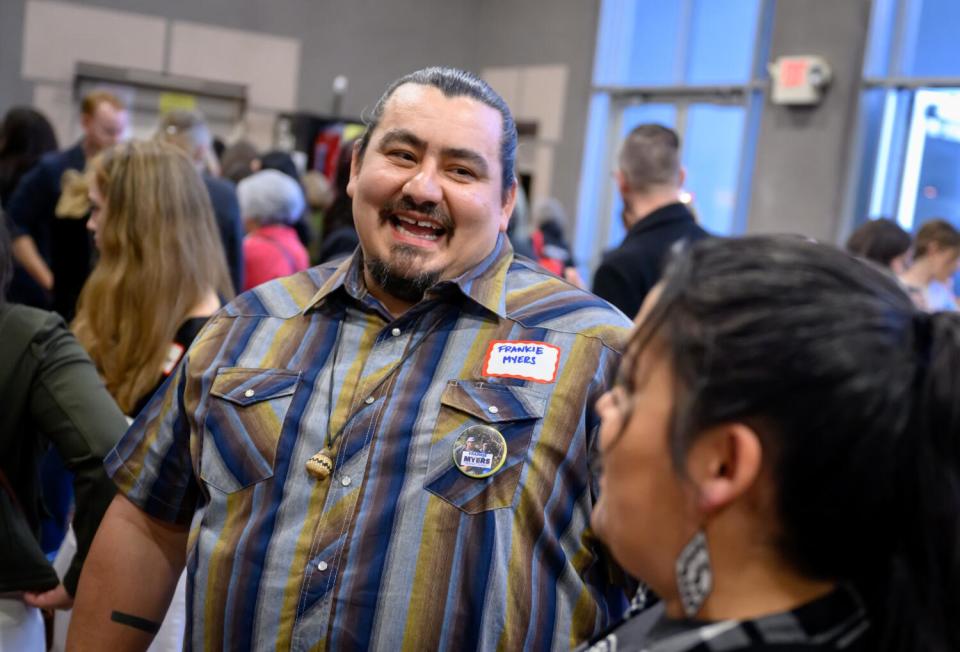 A man smiles while speaking to a woman at an event.