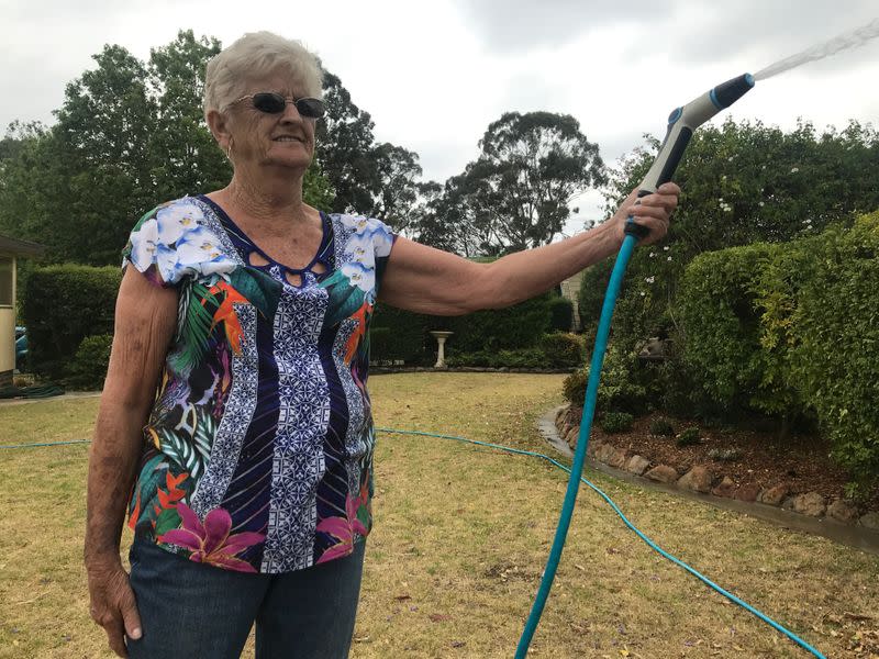 Diane Baxter hoses her garden as she did on Saturday to protect her home when raging bushfires swept past her home town of Yanderra