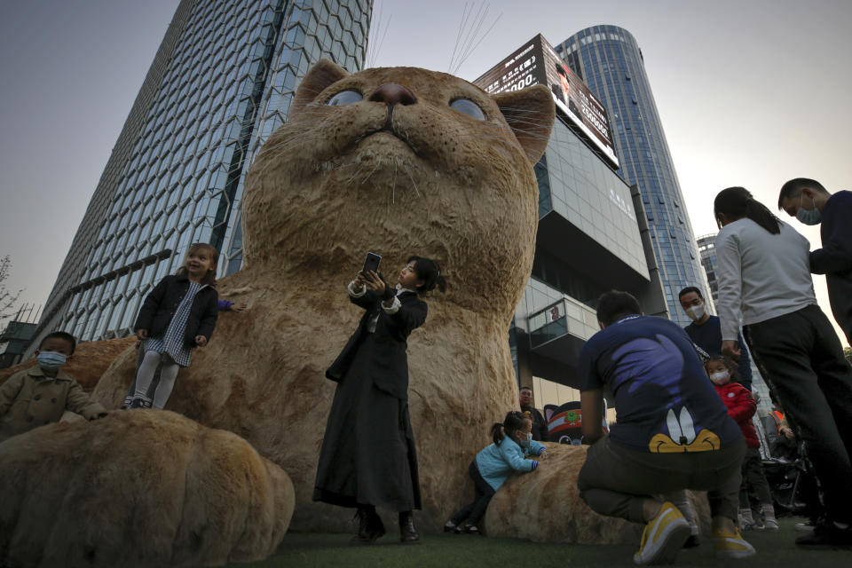 A woman takes a selfie as visitors wearing face masks to help curb the spread of the coronavirus gather near a giant cat structure on display at a commercial office building in Beijing, Sunday, Oct. 18, 2020. (AP Photo/Andy Wong)