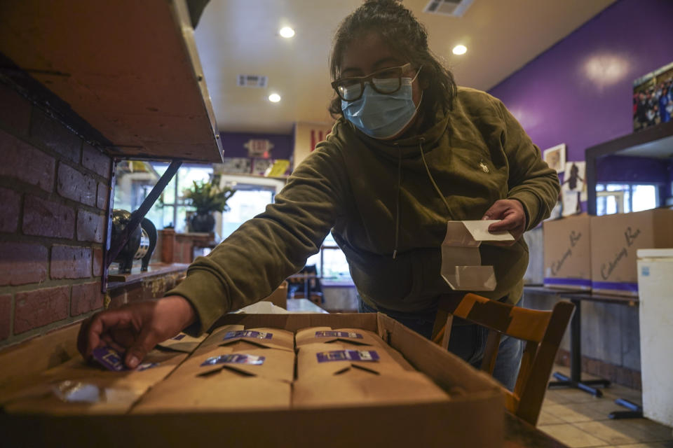 Yajaira Saavedra place stickers reading "La Morada Bx Mutual Aid Kitchen" on food boxes in her restaurant being prepared for distribution in her South Bronx neighborhood, Wednesday Oct. 28, 2020, in New York. Saavedra, 32, and her parents Natalia Méndez and Antonio Saavedra own La Morada, an award winning Mexican restaurant that reopened and also turned its operation into to a soup kitchen during the coronavirus pandemic, serving 650 meals daily. (AP Photo/Bebeto Matthews)