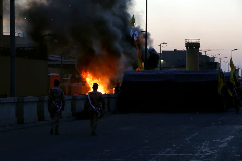 Iraqi security forces walk as the Hashd al-Shaabi (paramilitary forces) fighters set the U.S. Embassy wall on fire, as they protest to condemn air strikes on their bases, in Baghdad