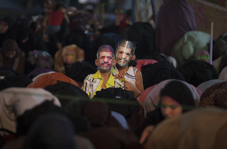 Two Egyptian girls wearing masks with pictures of Morsi, stand next to supporters of Egypt's ousted President Mohammed Morsi praying outside Rabaah al-Adawiya mosque, where protesters have installed a camp and hold daily rallies at Nasr City in Cairo, Egypt, Thursday, Aug. 1, 2013. (AP Photo/Khalil Hamra)