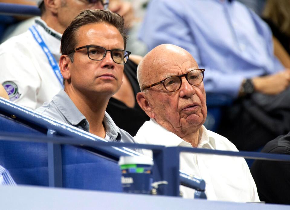 A young man and his father sit in the stands watching a tennis match.