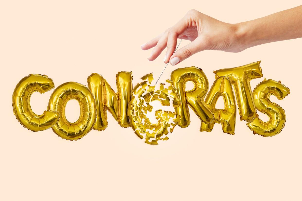 Balloon letters that spell out "Congrats" with a hand holding a needle popping the G