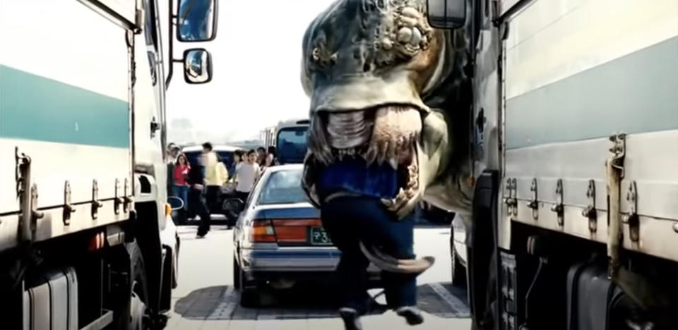 A giant creature grabs a person between two trucks in a busy street in a scene from the movie "The Host"