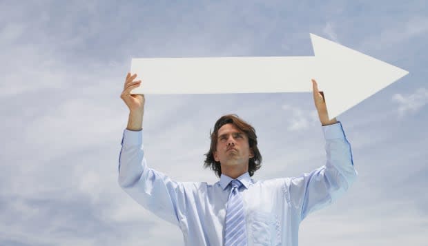 Businessman outdoors holding blank arrow with sky in background