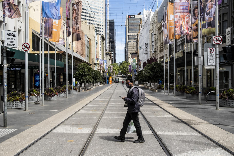 A man wearing a face mask as a preventive measure holds a cellphone while crossing Bourke street.Under the stage 4 restriction of lockdown due to the second wave of Covid 19, the city appears to be desolate with only a few people around for essential reasons. This harsh lockdown is unlikely to be eased on Sunday as expected. (Photo by Diego Fedele/SOPA Images/LightRocket via Getty Images)