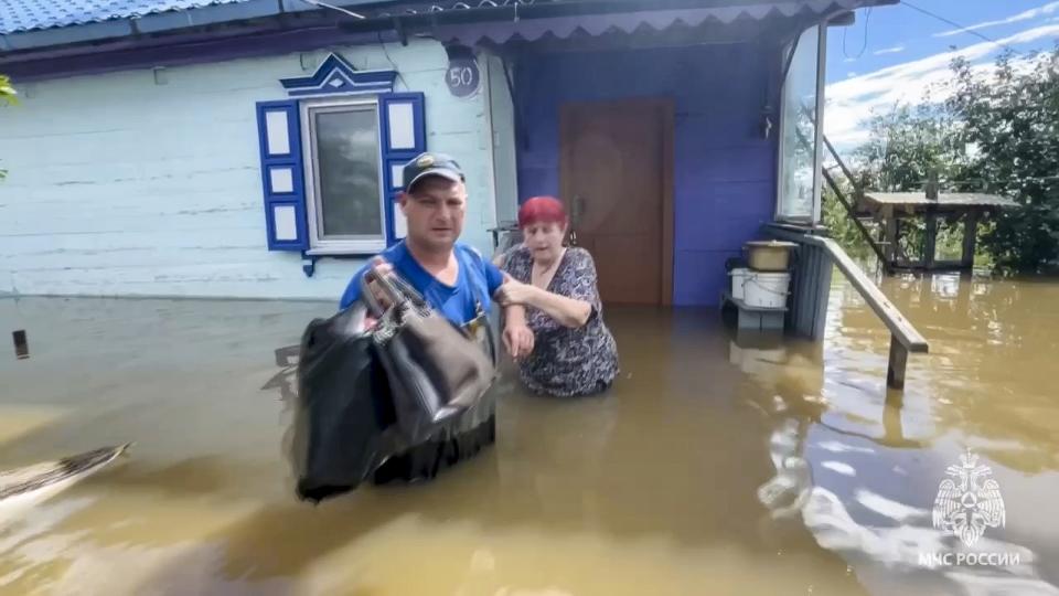 In this photo taken from video released by Russian Emergency Ministry Press Service on Sunday, Aug. 13, 2023, An Emergency service worker helps a woman to leave her house in a flooded village in Primorye region, Russia's Far East after heavy downpours flooded villages in the region in the aftermath of Typhoon Khanun. Russian emergency officials say over 2,000 people have been evacuated from flooded areas of the Primorye region in the country's Far East. (Russian Emergency Ministry Press Service via AP)
