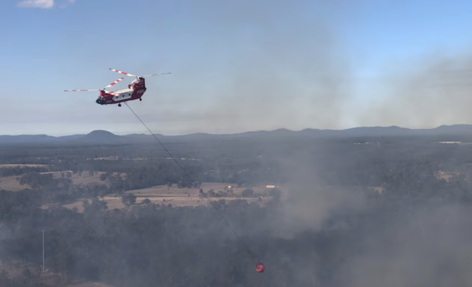 The RFS Chinook water-bombing helicopter is seen hovering above smoke and fire. 