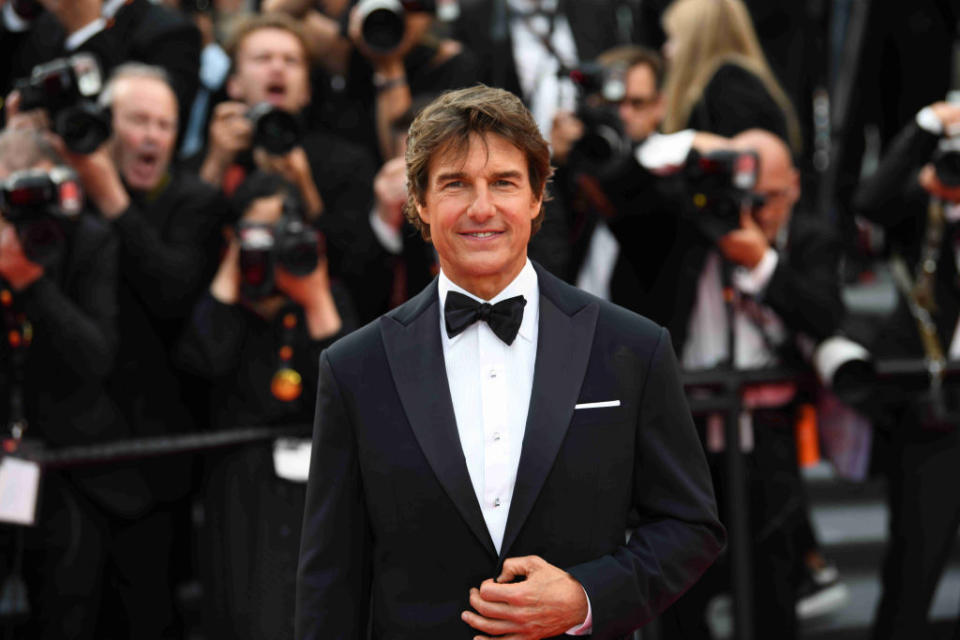 Close-up of Tom in a suit and bow tie with photographers behind him at a media event