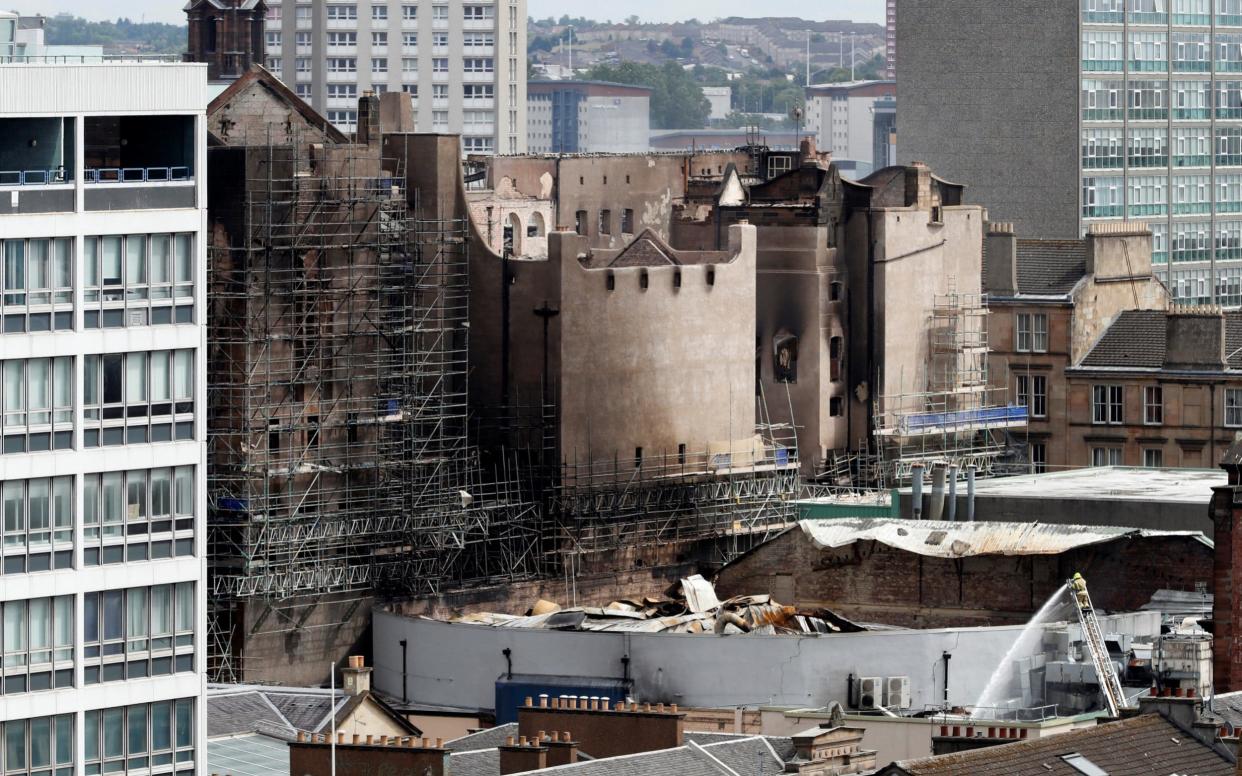 The charred remains of damaged buildings can be seen as firefighters continue to dampen fires in Glasgow - REUTERS