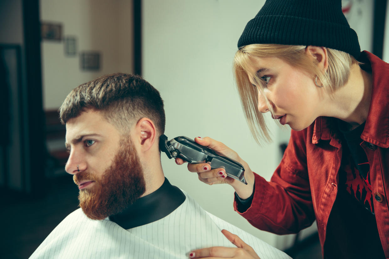 Client during beard shaving in barbershop. Female barber at salon. Gender equality. Woman in the male profession.