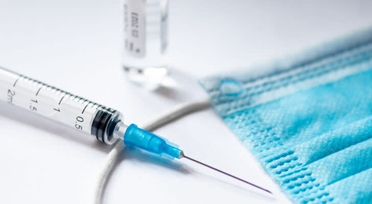 A syringe with a safety cap and a surgical mask laid out on a blank background