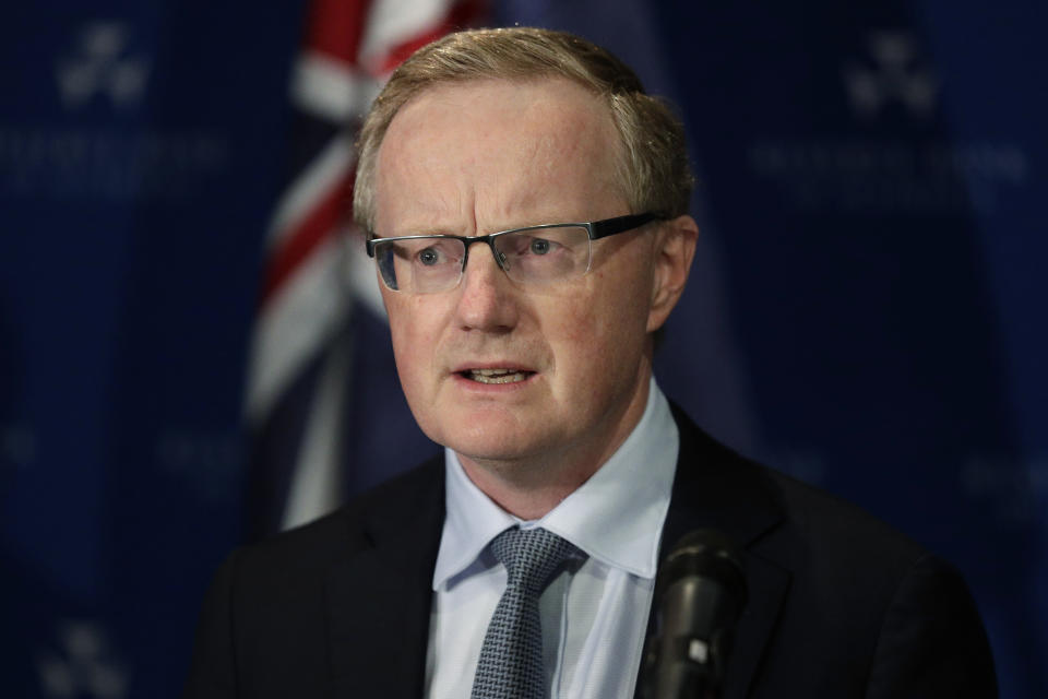 Reserve Bank governor Philip Lowe stands in front of an Australian flag. 