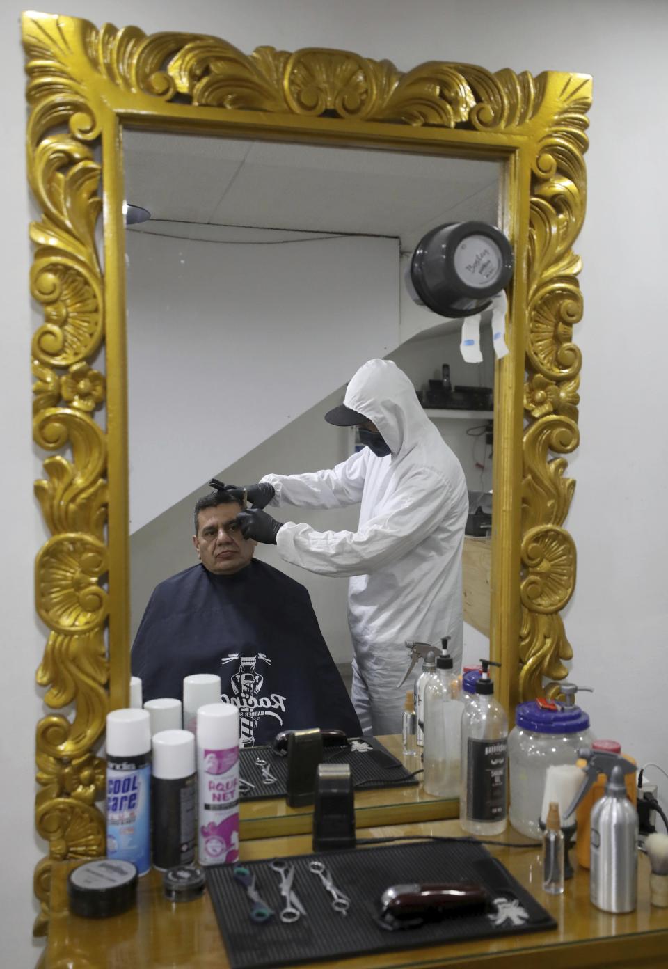 A barber in protective gear to curb the spread of the new coronavirus cuts the hair of a client in Bogota, Colombia, Tuesday, June 16, 2020. The Bogota city hall said that beauty salons, spas and barbershops are now allowed to reopen their doors every day at noon. (AP Photo/Fernando Vergara)