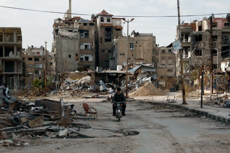 A man drives his motorbike past damaged buildings in Harasta, east of the Syrian capital Damascus on February 10, 2016