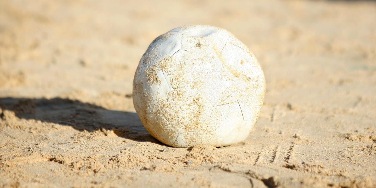 A soccer ball in the middle of a dirt road.