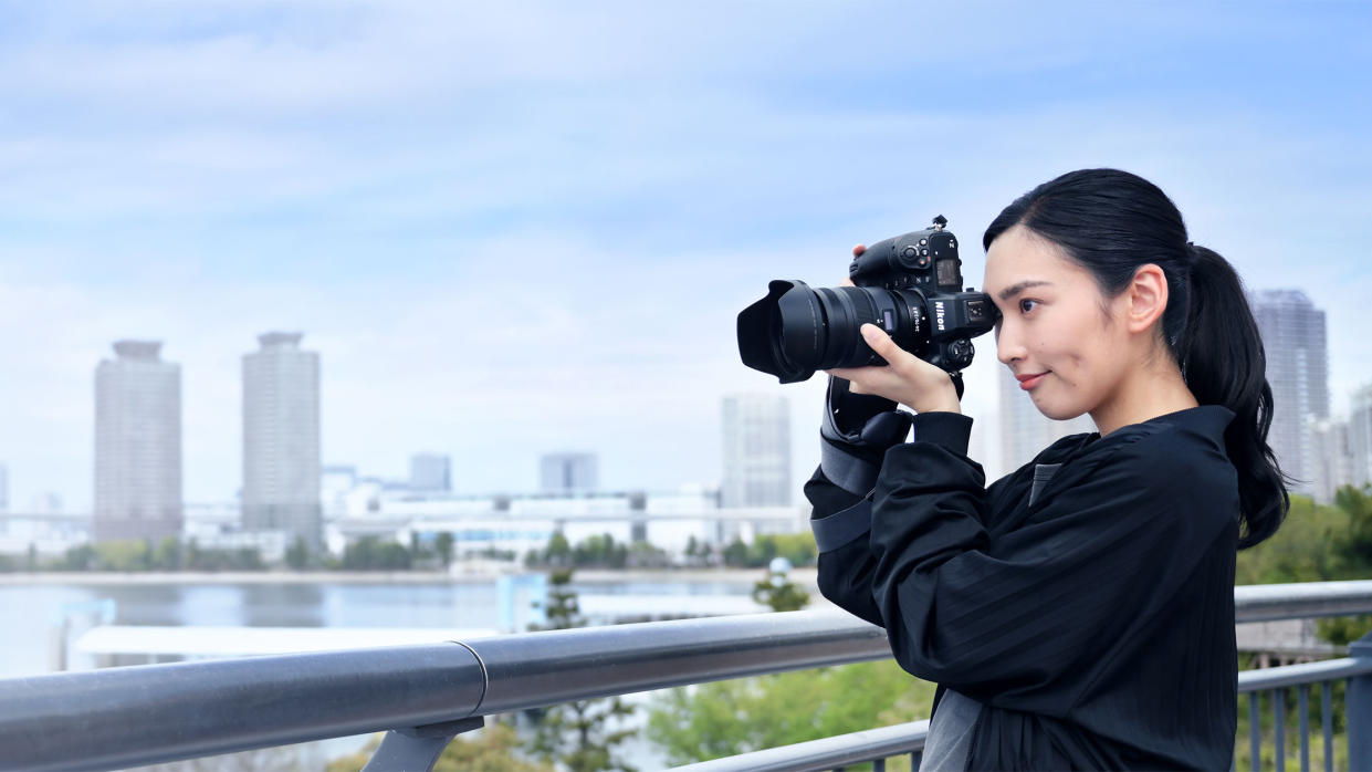  A female photographer uses a Nikon camera in front of a Japanese skyline. 