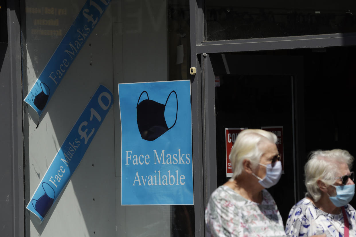 People walk past a sign advertising face masks for sale in a shop window in Kingston upon Thames, south west London, Monday, June 22, 2020. The two-metre social distancing rule will be under review as the UK relax coronavirus lockdown measures implemented to stem the spread of the virus. (AP Photo/Matt Dunham)