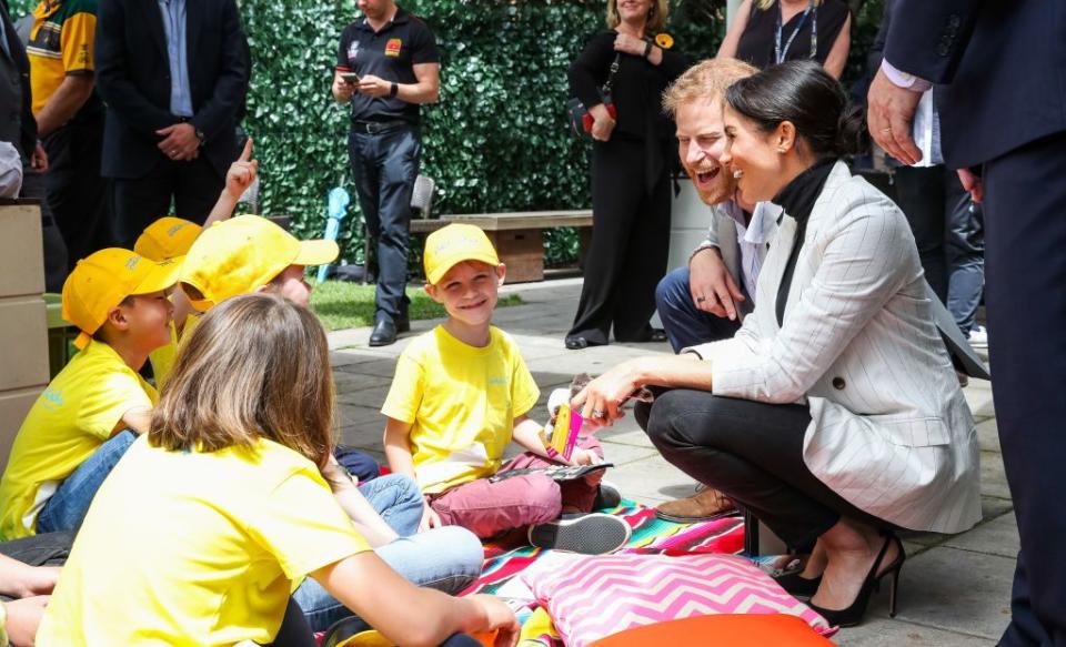 Harry and Meghan laugh while talking with young children in Sydney.