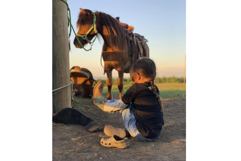 This 2021 photo provided by Elijah Benson shows Nashotay Young Bear pulling on his boots in Twin Buttes, ND. Born out of necessity and in mastering skills that came as horses transformed hunting, travel and warfare, rodeo has remained popular in Native American communities. Grandstands often play host to mini family reunions while Native cowboys and cowgirls show off their skills roping, riding and wrestling livestock. It's a lifestyle that's connected to nature and community. (Elijah Benson via AP)