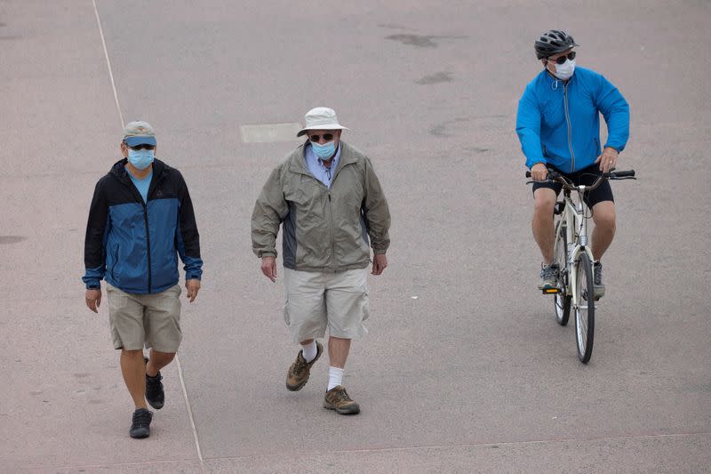 People wear face masks as they use the beach boardwalk during the outbreak of the coronavirus disease (COVID-19), in Huntington Beach, California