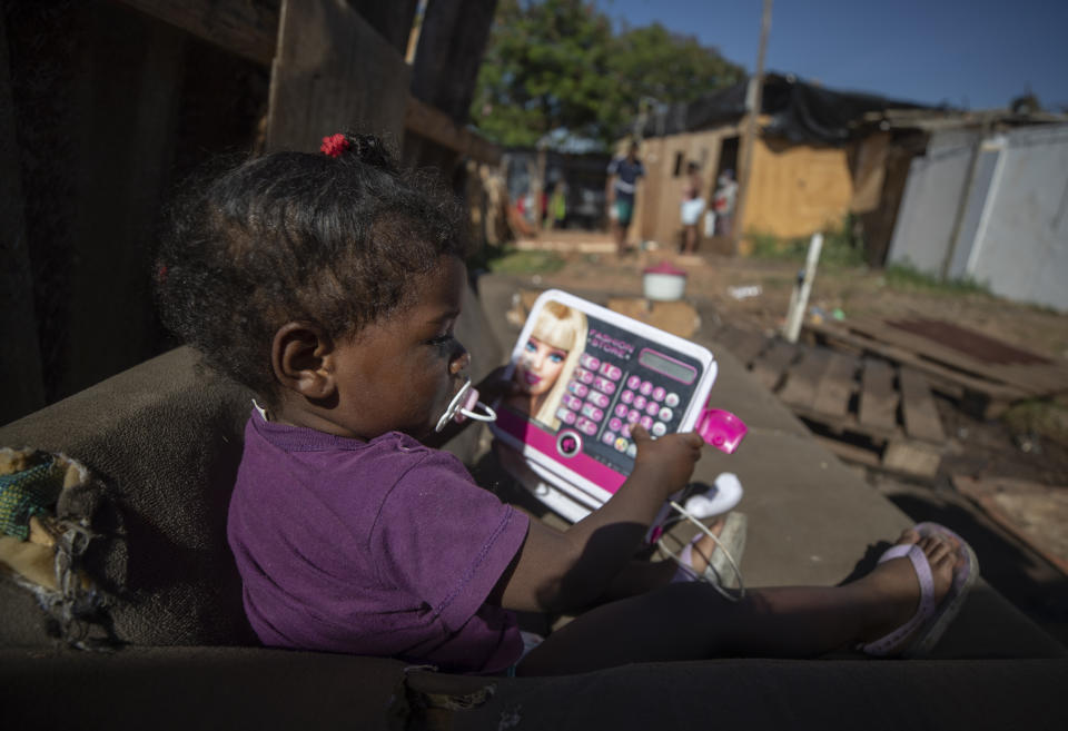 A girl plays with an educational electronic device in the Jardim Julieta squatter camp in Sao Paulo, Brazil, Thursday, July 23, 2020. The coronavirus had just hit the city when this parking lot for trucks became a favela, with dozens of shacks. Since the first wave of residents in mid-March, hundreds of families joined, with most having been evicted during the pandemic. (AP Photo/Andre Penner)