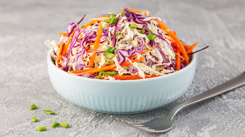 Bowl of coleslaw on gray background with fork