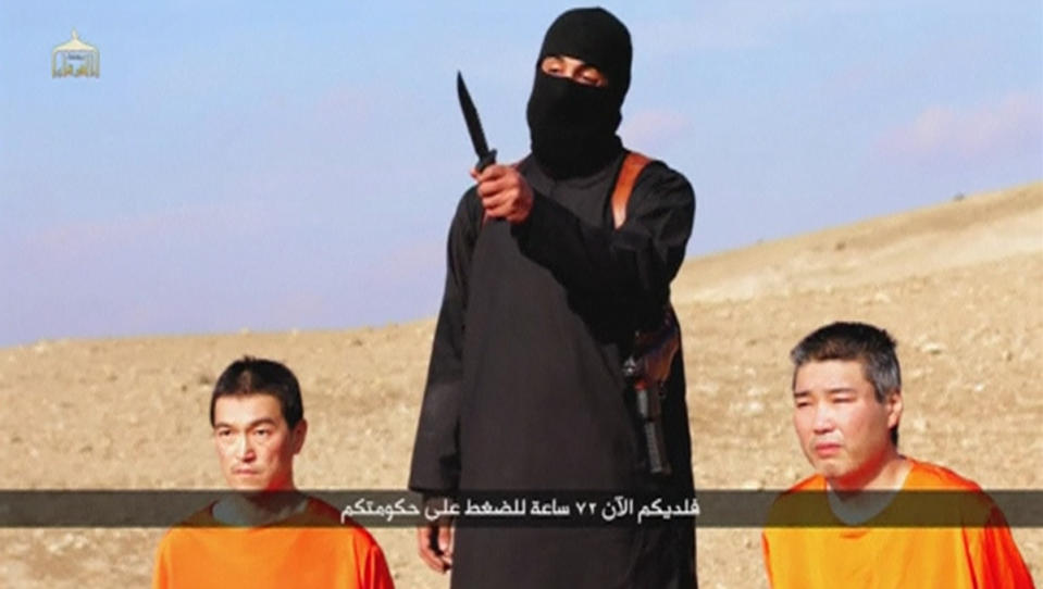 A masked person holding a knife speaks as he stands in between two kneeling men in this still image taken from an online video released by the militant Islamic State group