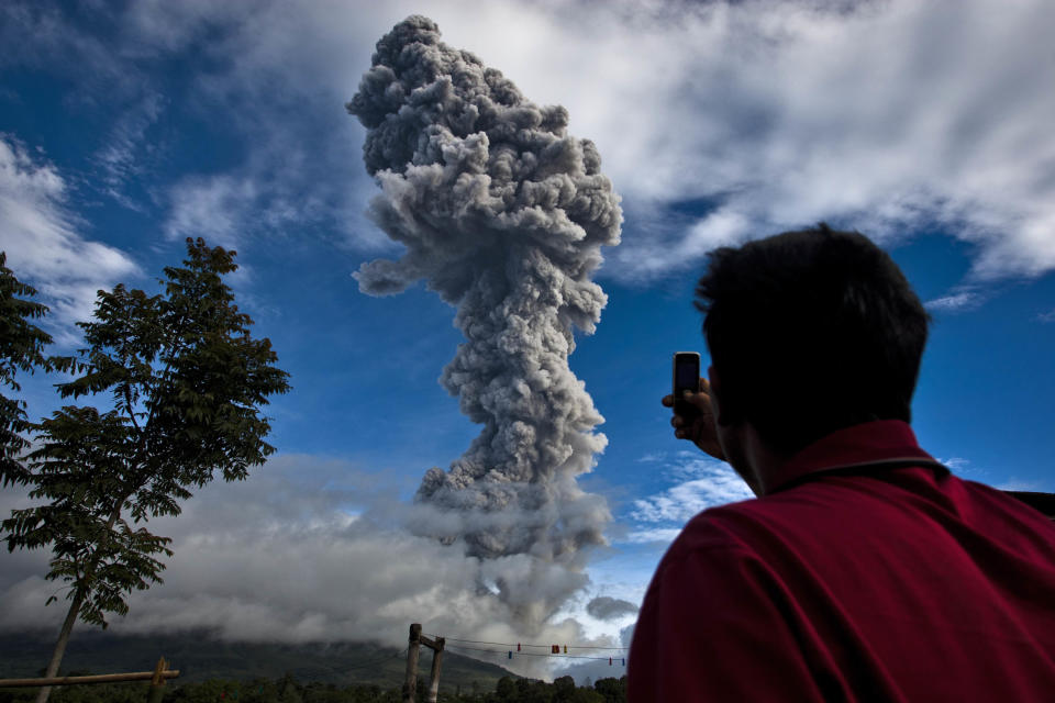 A man takes a picture with his phone as Mount Sinabung spews pyroclastic smoke seen from Tigapancur village on November 24, 2013 in Karo district, North Sumatra, Indonesia. Mount Sinabung, which has been intermittently erupting since September, has erupted eight times in just a few hours overnight. Officials have reported of rocks raining down over a large area, forcing thousands to flee their homes. The Indonesian government has called for people living within five kilometres (3.1 miles) of the volcano, on the northern tip of Sumatra Island, to evacuate their homes as the volcanology agency raised the alert level for the volcano to the highest point on a four-stage scale.  