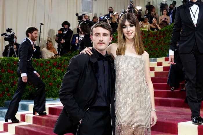 Paul Mescal and Daisy Edgar-Jones pose on the red carpet at a formal event. Paul wears a black suit, while Daisy is in a shimmering sleeveless dress