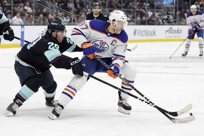 Edmonton Oilers center Connor McDavid (97) works to keep control of the puck under pressure from Seattle Kraken defenseman Vince Dunn (29) during the second period of an NHL hockey game, Saturday, March 18, 2023, in Seattle. (AP Photo/John Froschauer)