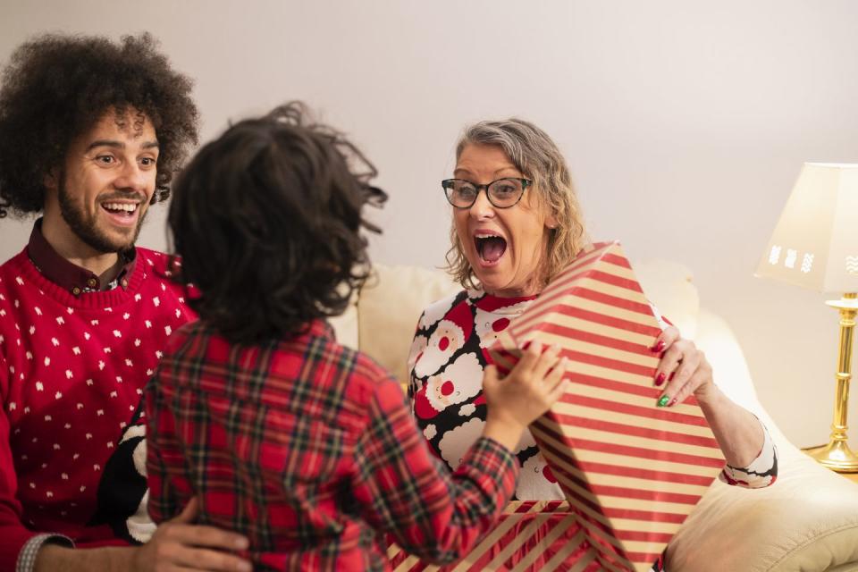 older woman sitting next to man on couch receiving a christmas gift from a young boy