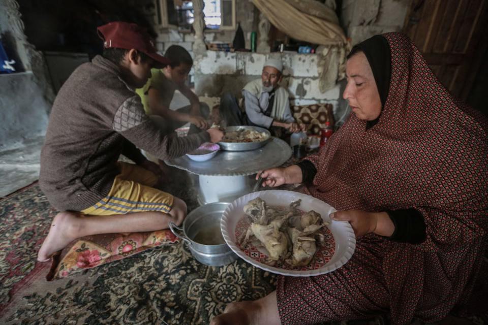 People sit on a colorful carpet on a makeshift table eating prepared food.