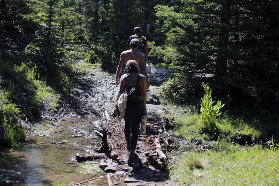 Rainbow Gathering participants walk across a creek using a handmade bridge on Friday, July 2, 2021, in the Carson National Forest, outside of Taos, N.M. More than 2,000 people have made the trek into the mountains of northern New Mexico as part of an annual counterculture gathering of the so-called Rainbow Family. While past congregations on national forest lands elsewhere have drawn as many as 20,000 people, this year’s festival appears to be more reserved. Members (AP Photo/Cedar Attanasio)