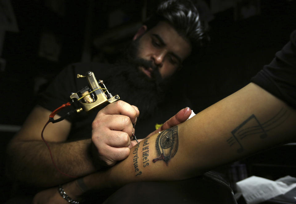 In this Tuesday. Oct. 23, 2018, photo, a man gets a tattoo on his arm in a tattoo studio in Baghdad, Iraq. One tattoo shop owner said he receives an average of 20 persons a year who want to cover their scars with tattoos, a nearly 30 percent increase from last year.(AP Photo/Hadi Mizban)