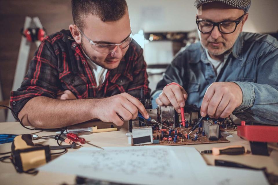 Two men tinker with electrical components.