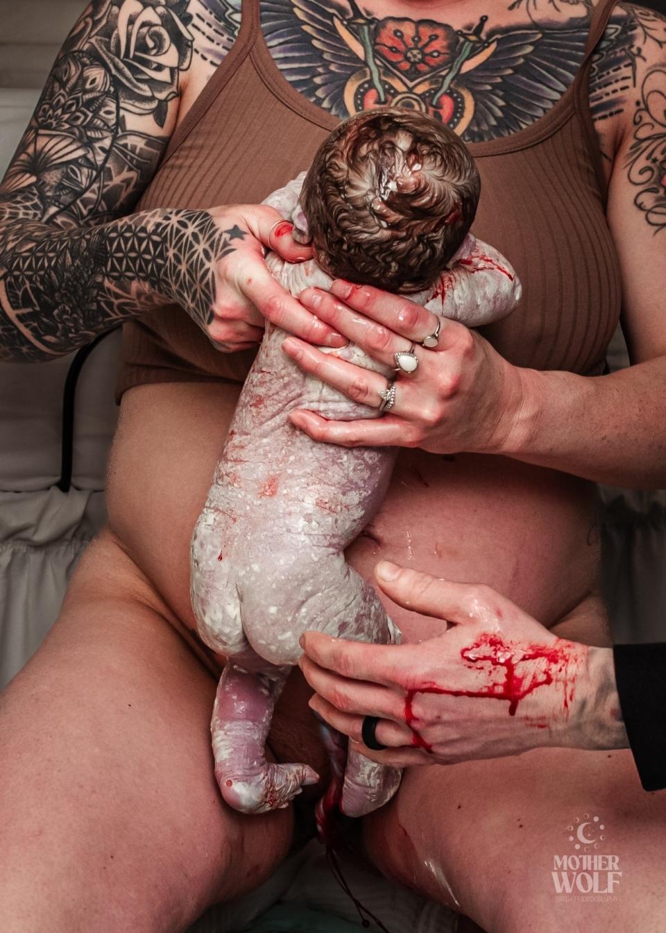 A newborn is cradled by a person with tattoos immediately after birth