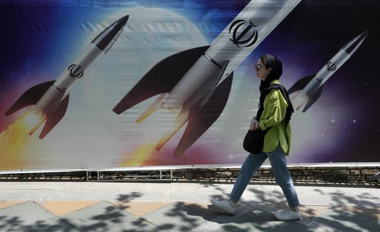 Una mujer camina junto a un cartel que muestra misiles siendo lanzados en el norte de Teherán, Irán, el viernes 19 de abril de 2024.