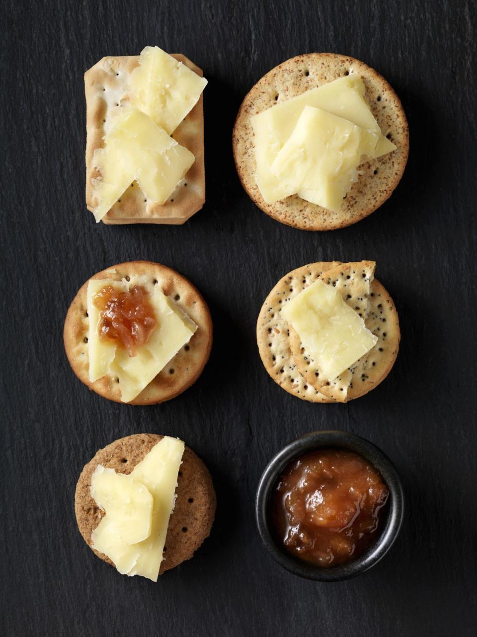 still life of variety of cheese crackers with cheddar cheese and chutney on black slate, overhead view