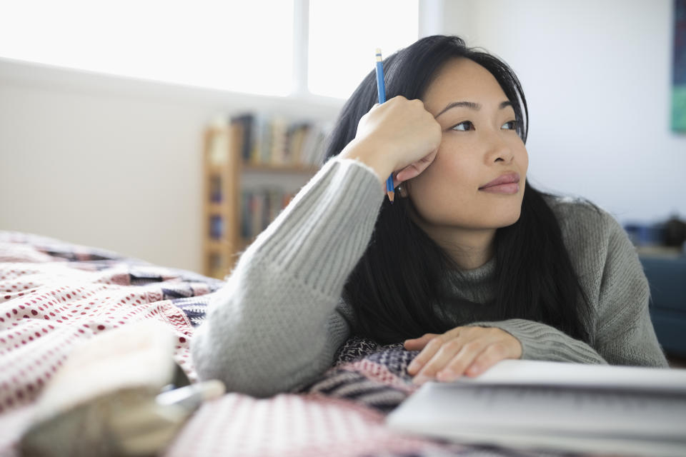 Pensive woman with pencil journaling, looking away on bed