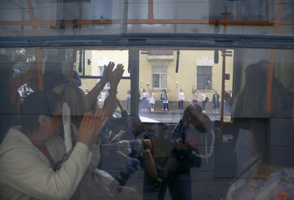 Belarusian passengers applaud through a bus window to women who taking part in a rally in solidarity with protesters injured in the latest rallies against the results of the country's presidential election while two men on a balcony greet them in Minsk, Belarus, Thursday, Aug. 13, 2020. Hundreds of people were back on the streets of Belarus' capital on Thursday morning, forming long "lines of solidarity" in protest against an election they say was rigged to extend the rule of the country's authoritarian leader and against a crackdown on rallies that followed the vote. (AP Photo/Sergei Grits)