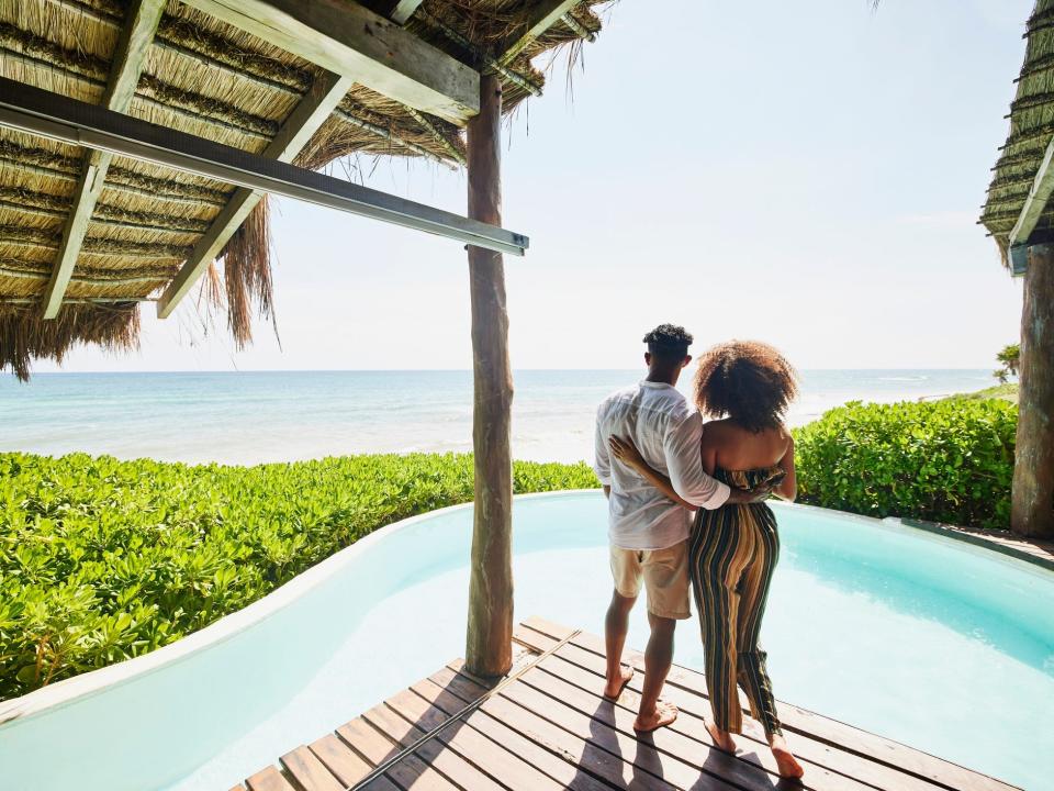 Couple standing poolside at luxury tropical beachfront villa looking at view
