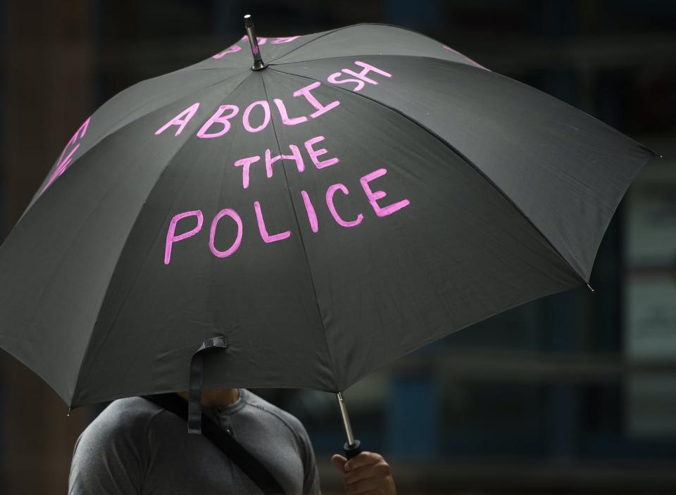 A woman carries an umbrella outside a protest to defund the police in front of Toronto Police Service headquarters in July 2020. Police budgets have increased, not decreased, since then. THE CANADIAN PRESS/Nathan Denette