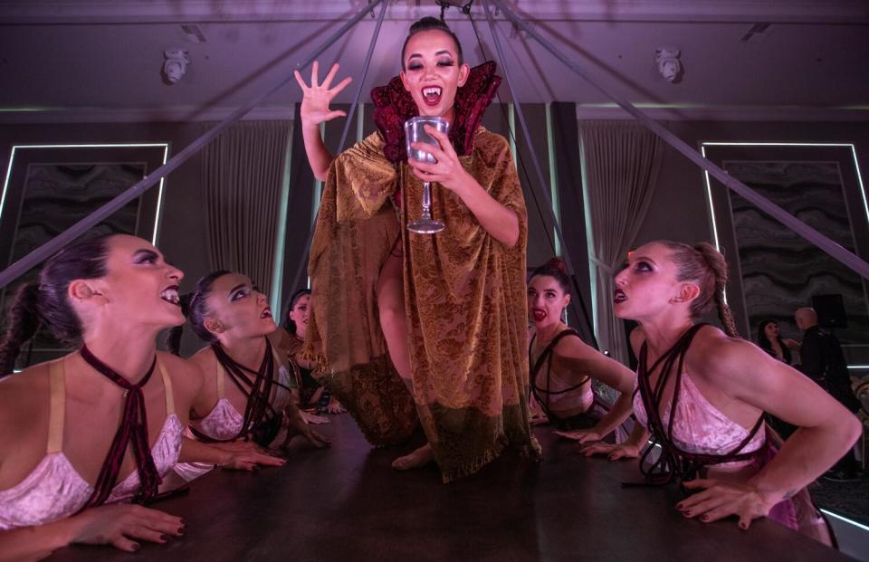 Frankie Tan holds up a goblet while several women sit at a table and look up at her.