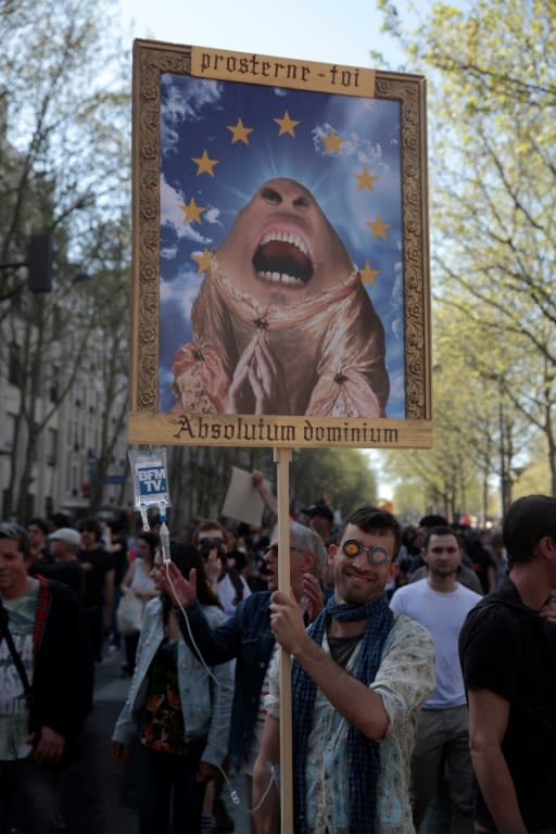 A protester holding a placard showing a caricature of the French president and reading "Absolute Power" in Latin, takes part in a demonstration on April 19, 2018 in Paris against government policies amid a rail strike and student sit-ins